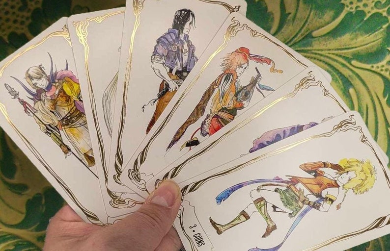 May include: A set of five tarot cards featuring illustrations of people in various poses. The cards are white with gold trim and feature a variety of colors in the illustrations. The cards are fanned out in a hand.