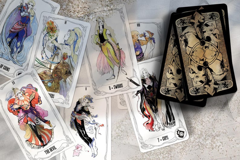 May include: A set of tarot cards featuring illustrations of characters from the Final Fantasy video game series. The cards are white with black borders and feature detailed artwork. The cards are laid out on a white surface.