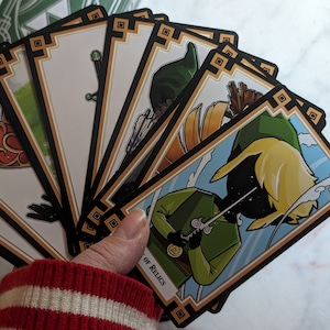 May include: A set of playing cards featuring a cartoon illustration of Link from the Legend of Zelda video game series. The cards are black and gold with a decorative border. The card in the foreground shows Link holding a sword and has the text "Of Relics" on the bottom.