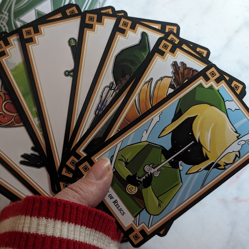 May include: A set of playing cards featuring a cartoon illustration of Link from the Legend of Zelda video game series. The cards are black and gold with a decorative border. The card in the foreground shows Link holding a sword and has the text "Of Relics" on the bottom.