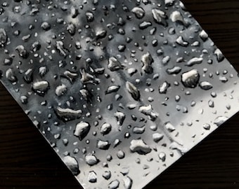 Könnte beinhalten: Nahaufnahme einer silbernen Oberfläche, die mit Wassertropfen bedeckt ist. Die Tropfen sind rund und reflektieren das Licht, wodurch ein schimmernder Effekt entsteht.