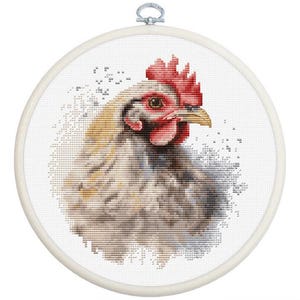 以下が含まれることがあります： 横向きの鶏の頭部をクロスステッチで刺繍した作品。鮮やかな赤色のトサカと肉垂、黄色のくちばし、白、グレー、ベージュの色合いの羽が特徴です。デザインは円形の木製刺繍枠の中央に配置されています。