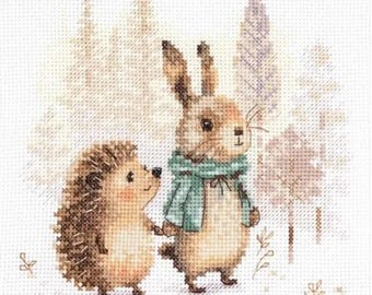 Könnte beinhalten: Ein Kreuzstich-Stickmuster mit einem braunen Igel und einem braunen Hasen, der einen hellen türkisfarbenen Schal trägt. Die Tiere stehen nebeneinander in einer Waldlandschaft mit blassen, gedämpften Bäumen auf einem weißen Stoffgitter.