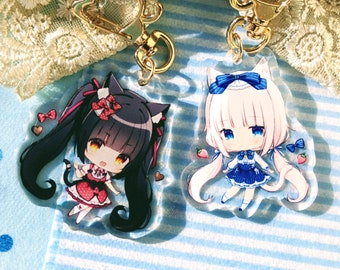 Könnte beinhalten: Zwei Anime-Charakter-Schlüsselanhänger mit goldenen Ketten. Der Schlüsselanhänger links zeigt ein schwarzes Katzenmädchen in rot-weißer Kleidung. Der Schlüsselanhänger rechts zeigt ein weißes Katzenmädchen in blau-weißer Kleidung.