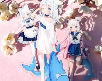 Puede incluir: Tres soportes de acrílico con personajes de anime. El primer personaje es una chica con el pelo largo y blanco, que lleva una camisa blanca con el texto "S-style" en ella. El segundo personaje es una chica con el pelo largo y blanco y un vestido azul. El tercer personaje es una chica con el pelo largo y blanco y un vestido azul. Los soportes están sobre un fondo rosa.