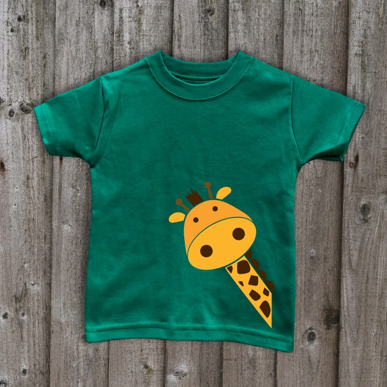 May include: A green t-shirt with a cartoon giraffe peeking out from the bottom left corner. The giraffe is yellow with brown spots and has a friendly expression.