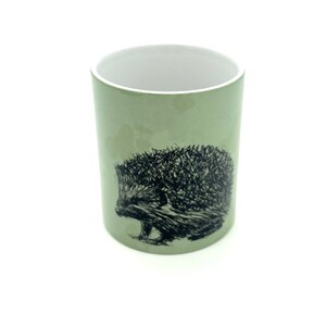 May include: A green ceramic mug with a black and white illustration of a hedgehog on the side.