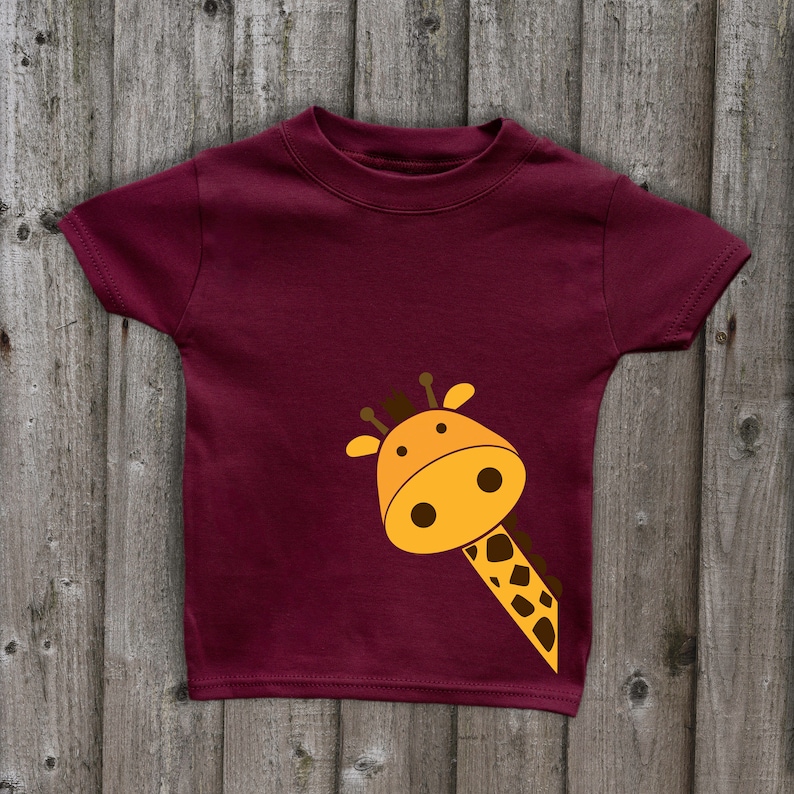 May include: A maroon t-shirt with a cartoon giraffe peeking out from the bottom right corner. The giraffe is yellow with brown spots and has a friendly expression.