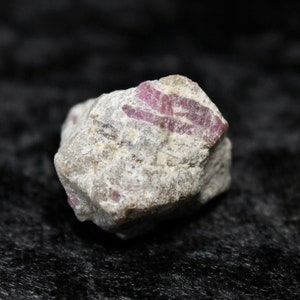 May include: A rough, grey rock with streaks of pink ruby. The rock is about the size of a golf ball.