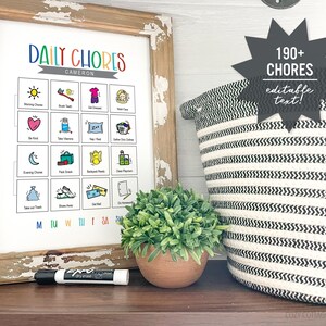 May include: A printable chore chart with colorful illustrations and the text "DAILY CHORES" and "CAMERON". The chart is framed in a rustic wooden frame and is sitting on a wooden surface. A black dry-erase marker is next to the chart. A black and white striped basket is in the background.