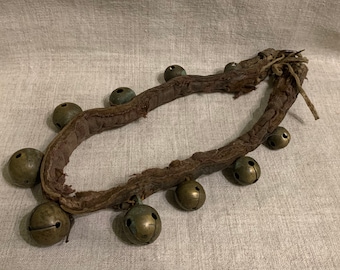 May include: A vintage leather strap with multiple brass bells attached. The strap is worn and has a rustic appearance.
