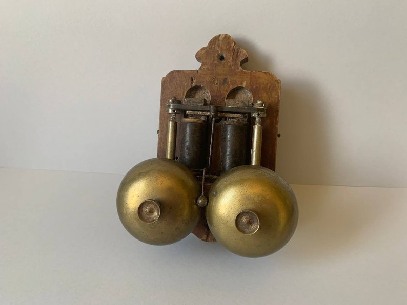 May include: Antique wooden wall mounted doorbell with two brass bells. The doorbell has a wooden frame and two brass bells.