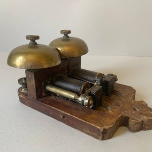 May include: Antique brass double bell door chime with a wooden base. The chime has two brass bells and a wooden base with a decorative design.