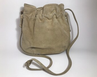 May include: A light brown suede bucket bag with a long adjustable strap. The bag has a drawstring closure and a slouchy, casual look.