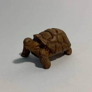 Op de afbeelding: Een klein, houten beeldje van een schildpad. De schildpad is bruin en heeft een gedetailleerd schild.
