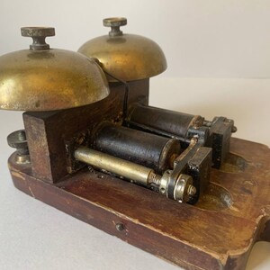 May include: Antique double bell door chime with brass bells and a wooden base. The chime has two black metal coils and a brass mechanism.