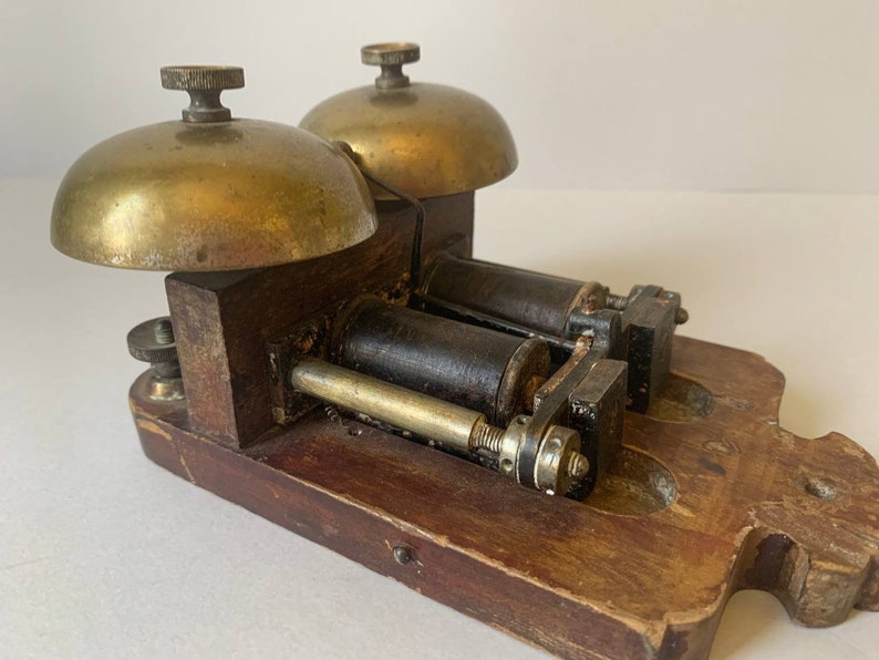 May include: Antique double bell door chime with brass bells and a wooden base. The chime has two black metal coils and a brass mechanism.