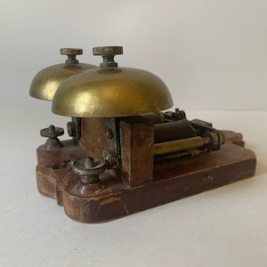 May include: Antique brass double bell door chime with a wooden base. The chime has two brass bells with a mechanism in the center.