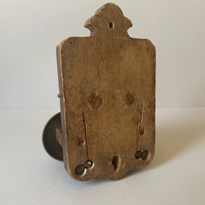 May include: A wooden wall mount with a decorative design and a metal ring on the bottom. The back of the mount is visible, showing the wood grain and a few holes.