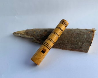 Puede incluir: Un silbato de madera con rayas negras, apoyado en un trozo de madera.