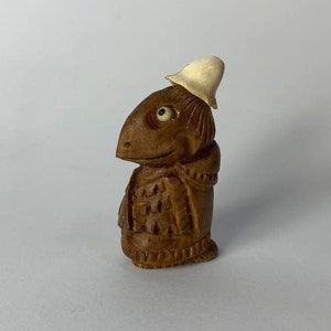 May include: A small wooden figurine of a creature wearing a white hat. The figurine is carved in detail and has a whimsical expression.