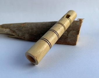 Puede incluir: Un silbato de madera con líneas negras talladas en la superficie. El silbato está sobre un trozo de madera.
