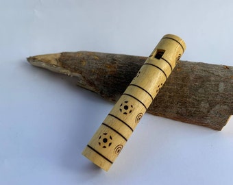Puede incluir: Una flauta de madera con un diseño decorativo de círculos y estrellas. La flauta es de color marrón claro y tiene un pequeño agujero cerca de la parte superior.