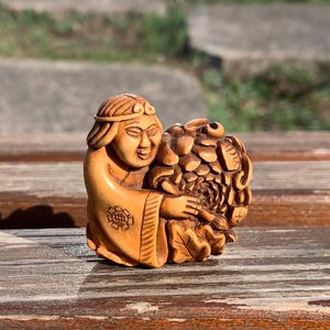 May include: A small, intricately carved wooden sculpture of a person holding a flower. The sculpture is made of light brown wood and has a detailed design.