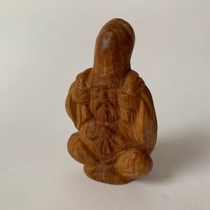 Op de afbeelding: Een klein, ingewikkeld gesneden houten beeldje van een zittend figuur met een lange baard en een gewaad. Het beeldje is gemaakt van lichtbruin hout en heeft een gedetailleerd ontwerp.