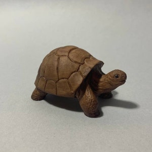 Op de afbeelding: Een klein, bruin houten schildpadbeeldje. De schildpad is gedetailleerd gesneden, met een getextureerde schild en een realistisch gezicht.