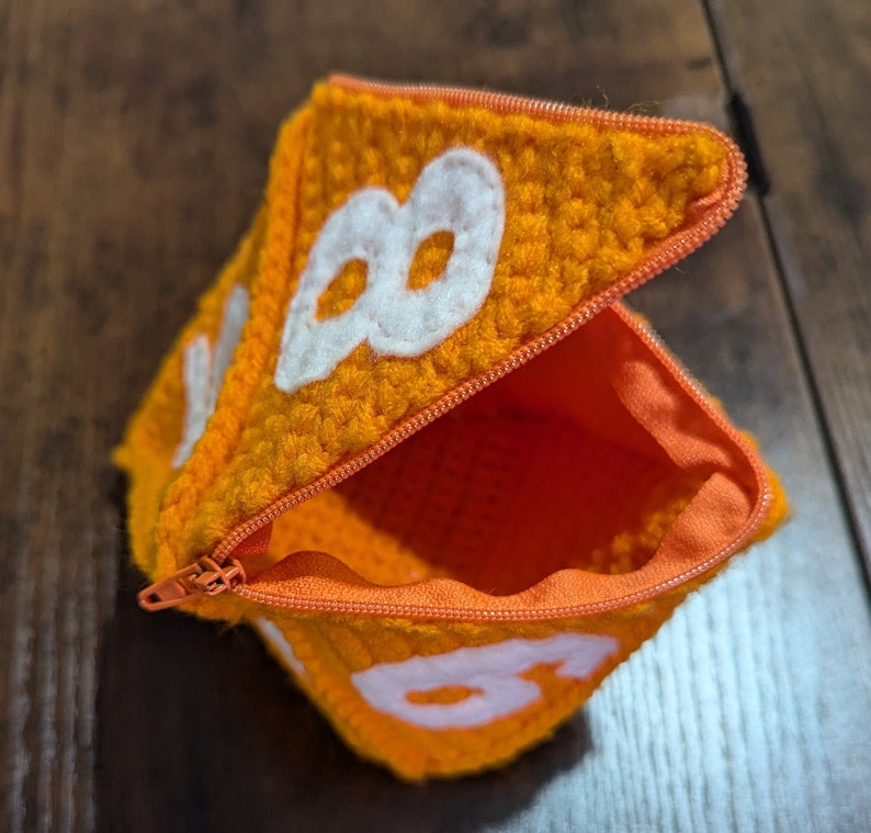 May include: Orange crocheted pouch with a zipper closure and white felt numbers 8 and 8 on the front.