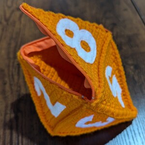 May include: Orange felt dice pouch with a zipper opening and white numbers 2, 4, 6, and 8 visible.