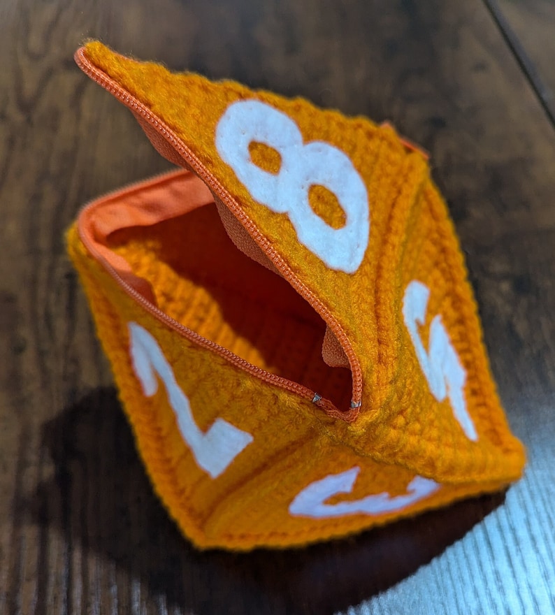 May include: Orange felt dice pouch with a zipper opening and white numbers 2, 4, 6, and 8 visible.