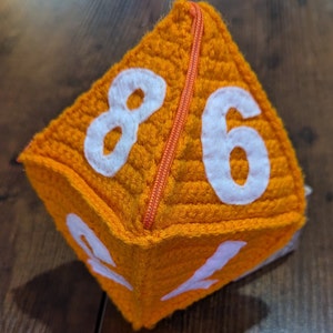 May include: A plush orange dice with white numbers 8, 6, 1, and 2. The dice has a zipper sewn down the middle.