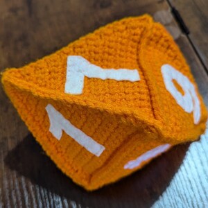 May include: A crocheted orange dice with white numbers 1 and 9 on the visible sides.