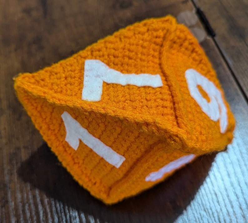 May include: A crocheted orange dice with white numbers 1 and 9 on the visible sides.