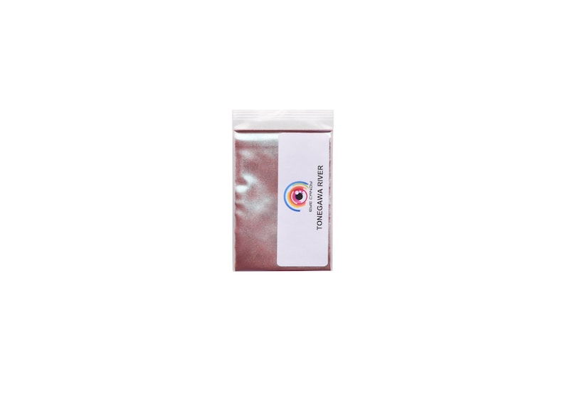 May include: A small, clear plastic bag filled with a shimmering, reddish-brown powder. A white label with the text "TONEGAWA RIVER" and a colorful eye logo is affixed to the bag. The bag is sealed at the top.