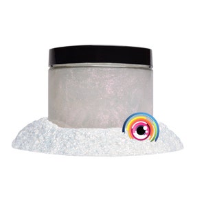 May include: A clear jar filled with iridescent white glitter. The jar has a black lid and is sitting on a pile of white glitter. A colorful eye with a rainbow design is in the glitter.