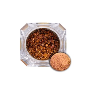 May include: A small jar of iridescent copper glitter with a scoop of glitter next to it.