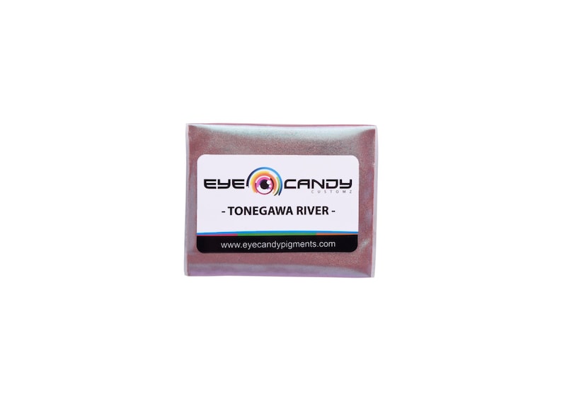 May include: A small, rectangular package of "TONEGAWA RIVER" eye candy pigments. The package has a white label with the brand name and a rainbow logo. The pigment inside appears to be a shimmering, reddish-brown color.