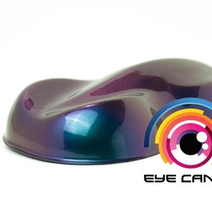 Puede incluir: Muestra de pintura brillante, iridiscente, púrpura y verde azulado. La pintura tiene una forma suave y curvada, con un degradado de colores. El logotipo "EYE CANDY" está en la esquina inferior derecha, con un diseño de ojo colorido.