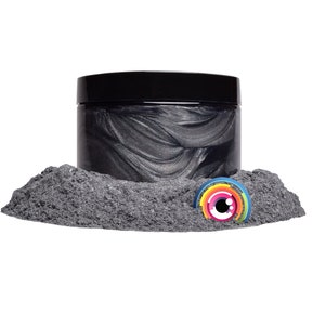 May include: A black jar of metallic silver paint with a small rainbow eye sticker on a pile of black powder.