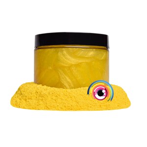 May include: A jar of yellow glitter with a black lid. The glitter is in a pile of yellow sand with a colorful eye sticker on top.