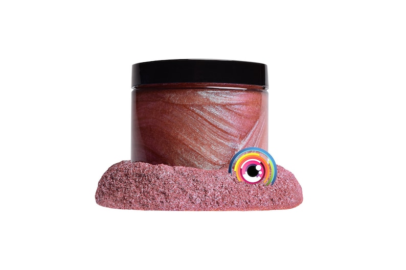 May include: A jar of shimmering, reddish-pink cosmetic product with a black lid. The jar sits on a bed of textured, pink material. A colorful, circular logo is partially visible.