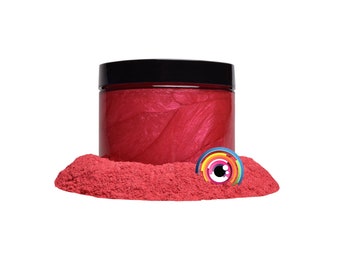 May include: A jar of red mica powder with a black lid. The powder is in a pile on a white surface.
