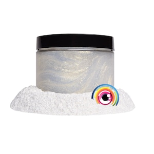 May include: A white jar with a black lid filled with iridescent glitter. The jar is sitting on a pile of white glitter.