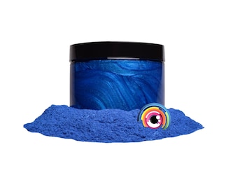 May include: A jar of blue iridescent mica powder with a black lid. The powder is spread out around the jar, creating a small pile.