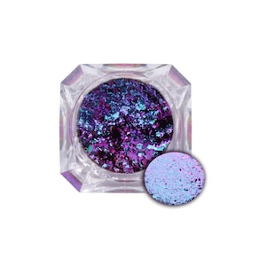 May include: A clear, faceted container filled with iridescent purple and blue flakes. A small, round sample of the flakes is next to the container. The flakes have a shimmering, multi-tonal appearance, reflecting light in various colors.