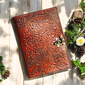 May include: A brown leather journal featuring a tree of life design and two wolves on the front. The journal has a brass clasp closure.