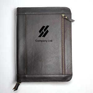 Op de afbeelding: Een bruin leren portfolio met rits met een zwart logo met de tekst "Company Ltd" en een zwart geometrisch ontwerp.